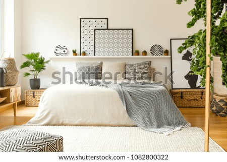 Warm bedroom interior with a comfy bed, patterned blanket and pillows, plants and modern graphics