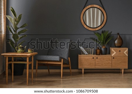 Sitting corner with wooden table, green cup and pot in a grey room interior with mirror and cabinet
