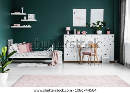 Posters on green wall in girl\'s bedroom interior with white bed and wooden pink chair at dressing table