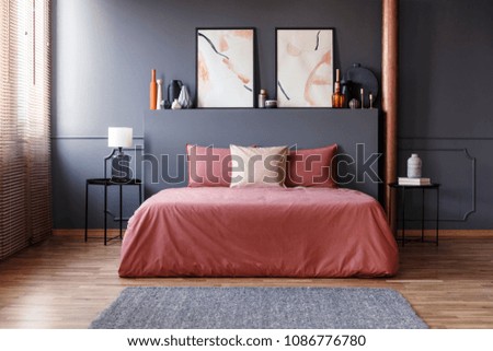 Real photo of a simple bedroom interior with dirty pink bedding on the bed standing against dark gray wall with molding, between two, metal bedside tables