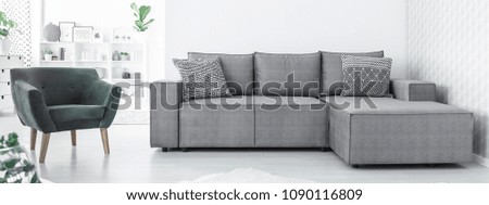 Grey corner sofa with two black and white cushions and green chair standing in white Scandinavian open space interior
