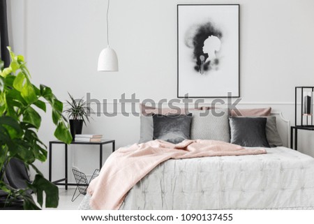 Gray and silver cushions lying on a bed with white sheets and pink blanket in feminine bedroom interior