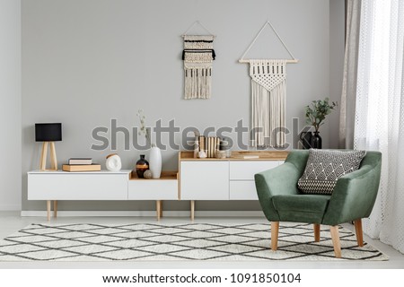 Green armchair on patterned carpet in bright living room interior with decor on the wall. Real photo