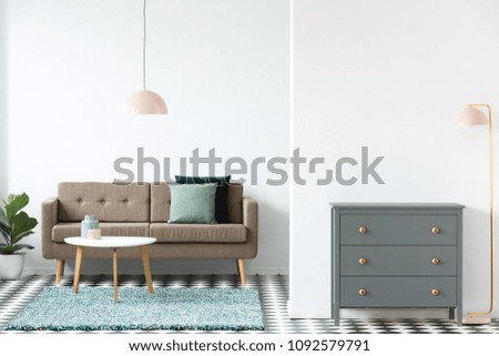 Pink lamp next to grey cabinet in retro living room interior with white table on rug near brown sofa