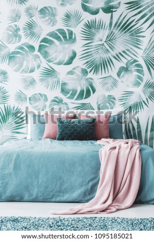 Bright room interior with powder pink blanket on bed and green and white leaf wallpaper