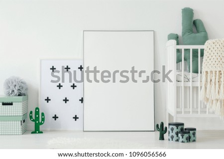 Mockup of white empty poster next to cradle in kid's room interior with cactus motif. Real photo wit a place for your graphic design