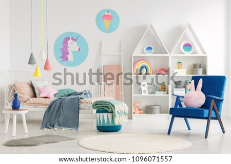 Sweet bedroom interior for a kid with a blue armchair, rabbit pillow, bed, unicorn, ice-cream posters and shelves
