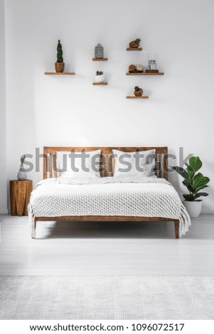 Wooden framed double bed with two pillows and a blanket, and small shelves above in a white bedroom interior. Real photo.