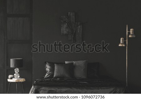Gold lamp next to bed in black bedroom interior with sculpture on dark wall