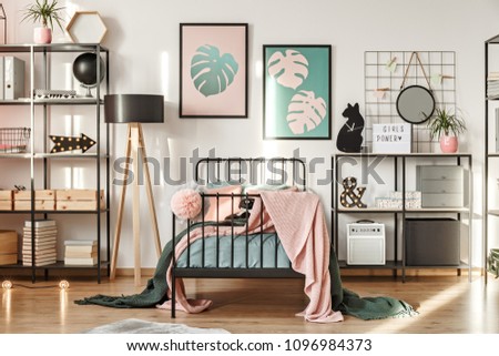Metal shelves with decorations, botanical posters and comfy bed in a girl bedroom interior