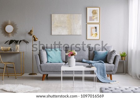 Flowers on table in grey flat interior with gold lamp next to settee against the wall with poster. Real photo