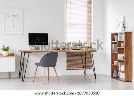 Grey chair at desk with computer monitor in minimal workspace interior with poster. Real photo