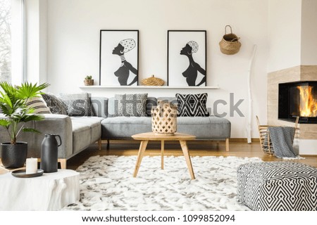 Patterned pouf next to wooden table in african living room interior with posters. Real photo