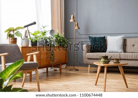 Wooden table in vintage living room interior with cabinet between sofa and armchair. Real photo