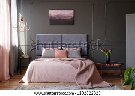 Tulips on copper table next to pink bed against grey wall with molding with poster in bedroom interior