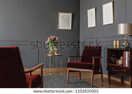 Elegant psychologist\'s office interior with two red armchairs facing each other between a golden table with flowers and vintage, wooden cabinet. Real photo