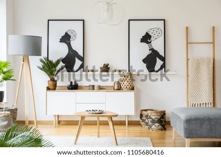 Black and white african posters above cabinet in living room interior with lamp and table. Real photo