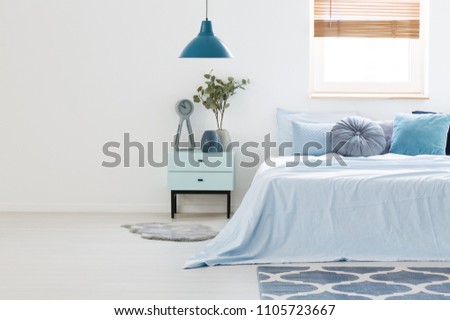 Real photo of a blue and white bedroom interior with wooden nightstand between a light blue bed and an empty wall. Paste your armchair here