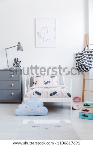 Blue cloud pillow in front of white bed next to grey cabinet in kid\'s bedroom interior. Real photo