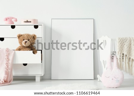 Plush toy in cabinet next to poster with mockup and cradle in baby\'s bedroom interior. Real photo. Place for your graphic