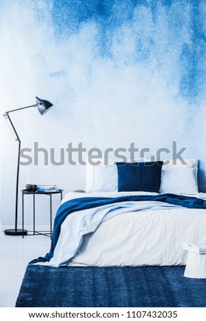 Navy blue carpet in front of bed next to lamp in bedroom interior with wallpaper