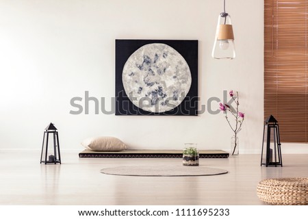 Bright and simple bedroom interior with asian style tatami mat bed, cherry blossom, moon painting on white wall and black lanterns. Real photo