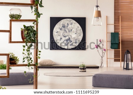 Moon painting above tatami mat bed in japanese style flat interior with ivy on wooden rack and ladder near the window. Real photo