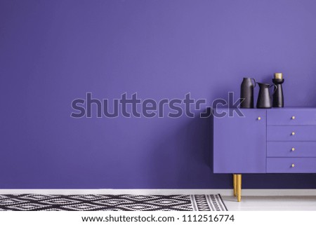 Black vase on violet cabinet against the wall with copy space in minimal living room interior with carpet