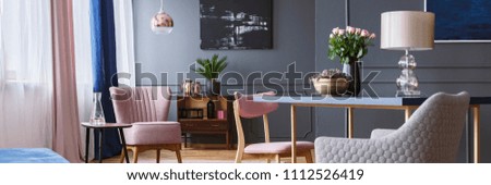 Open space living room interior with poster on grey wall with wainscoting, window with drapes and pink armchair