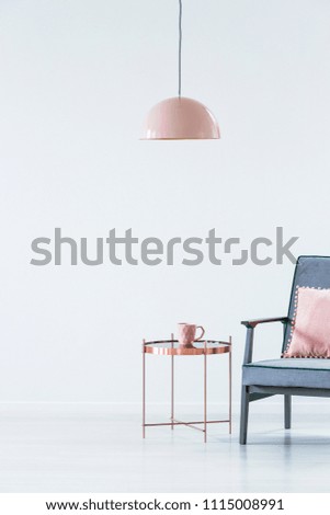 Pink lamp above copper table next to a blue armchair in pastel living room interior with copy space. Paste your armchair here