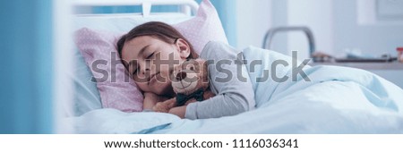Panorama portrait of a sick little girl sleeping in a hospital bed with a teddy bear - view through the door