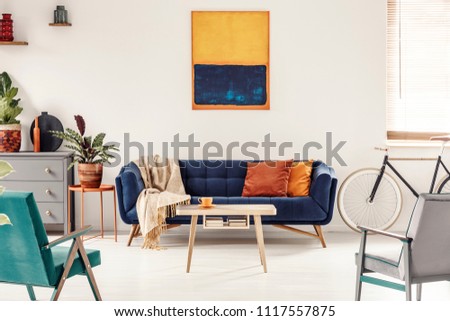 Yellow and navy blue painting above sofa in colorful living room interior with bike. Real photo