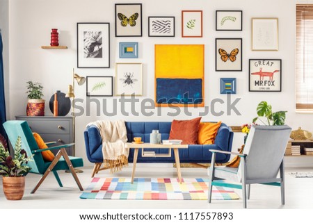 Grey and green armchair in artistic living room interior with gallery above navy blue settee. Real photo