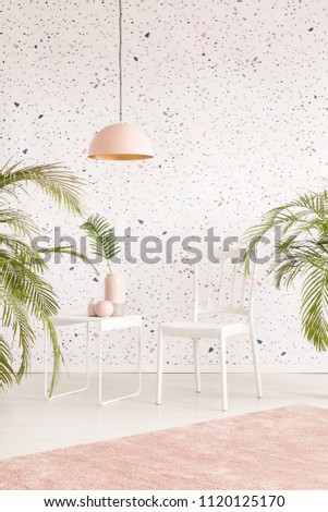 White chair between plants in pastel living room interior with lamp above carpet. Real photo