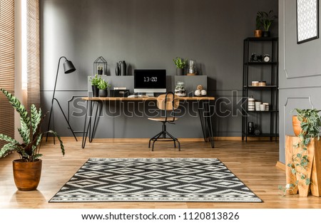 Patterned carpet and plants in scandi grey home office interior with wooden chair at desk