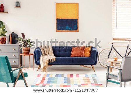 Yellow and navy blue painting above sofa in modern living room interior with bike. Real photo
