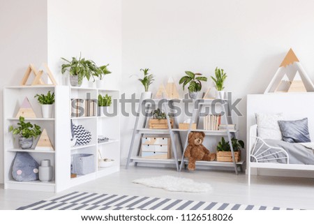 Plants on shelves in scandi grey bedroom interior with striped carpet near bed. Real photo