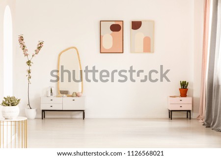 Mirror on white cabinet and plant in bright dressing room interior with posters and copy space. Real photo with a place for your bed