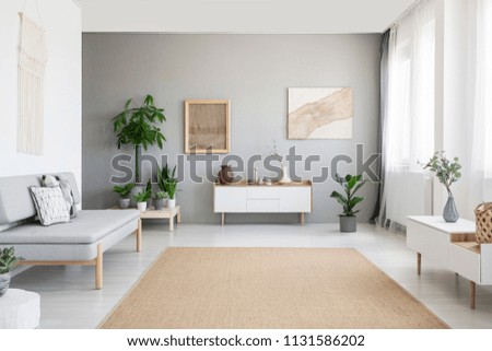 Burlap artwork on grey wall above white cupboard in bright living room interior with sofa and carpet. Real photo