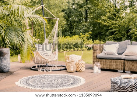 Pillows on hammock on terrace with round rug and rattan sofa in the garden. Real photo