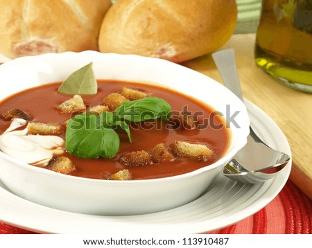 Closeup of garnished tomato soup with croutons and rolls in a background