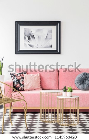 Pink sofa decorated with pillows, poster on the wall and golden tables in a living room interior. Real photo