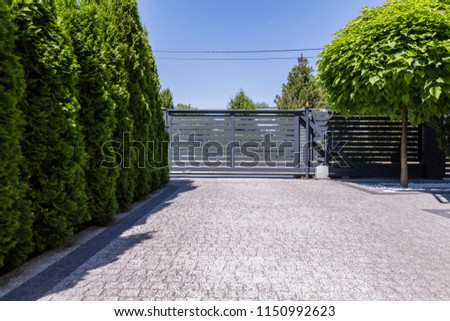 Green trees and grey entry gate to the property during summer. Real photo