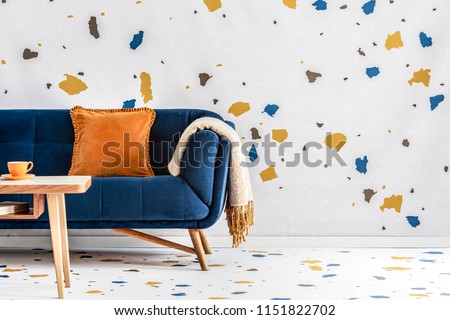Orange pillow and blanket on navy blue sofa in colorful living room interior with table. Real photo