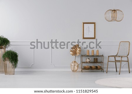 Real photo of living room interior with fresh plants, poster on wall, gold chair and small rack with decor and candles