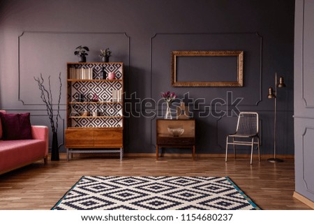 Patterned carpet in spacious grey retro living room interior with pink settee and gold chair. Real photo