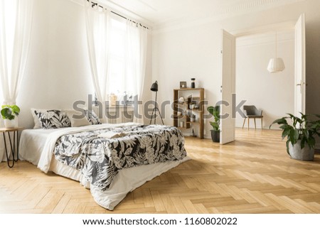 Stylish apartment interior with white walls and herringbone wooden floor. A view from a bedroom with a big bed to another room with an armchair. Real photo.