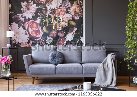Industrial golden pendant light and black furniture in a dark living room interior with floral wallpaper and a gray couch