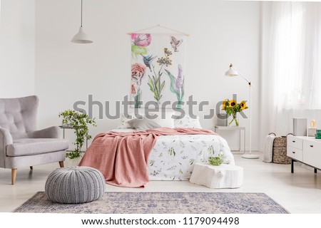 Nature lover\'s bright bedroom interior with a wall art of flowers and birds painted on a fabric above a bed which is dressed in green plants pattern on white linen. Real photo.