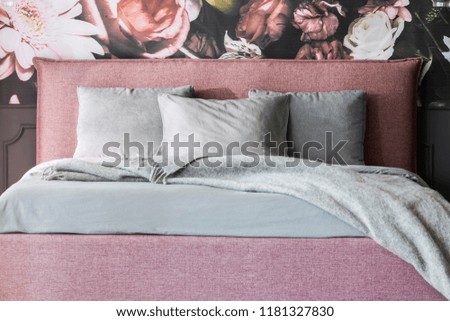 Grey blanket and cushions on pink bed in feminine bedroom interior with flowers wallpaper. Real photo